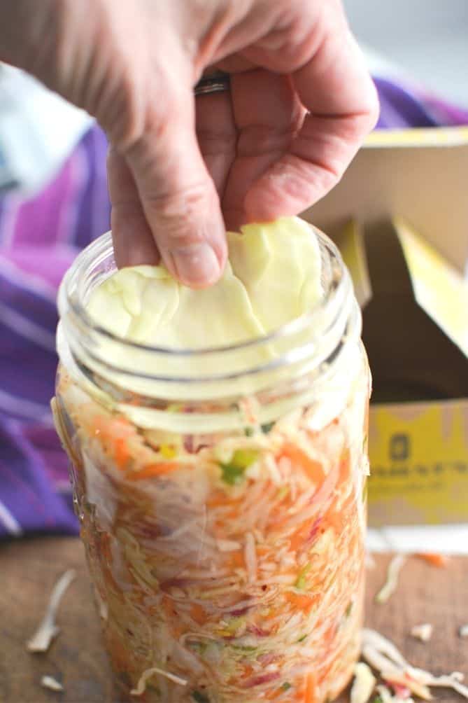 Cabbage leaf places into top of jar of kimchi. | MakeSauerkraut.com