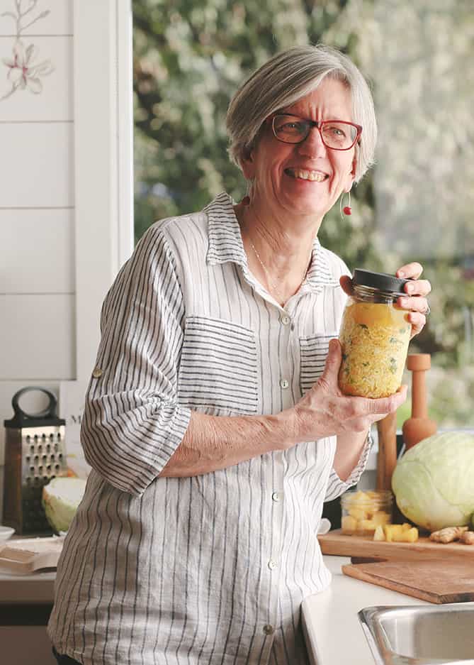 Woman in striped shirt holding jar of sauerkraut.Woman in striped shirt holding Kitchen Scale sign above hear. | MakeSauerkraut.com
