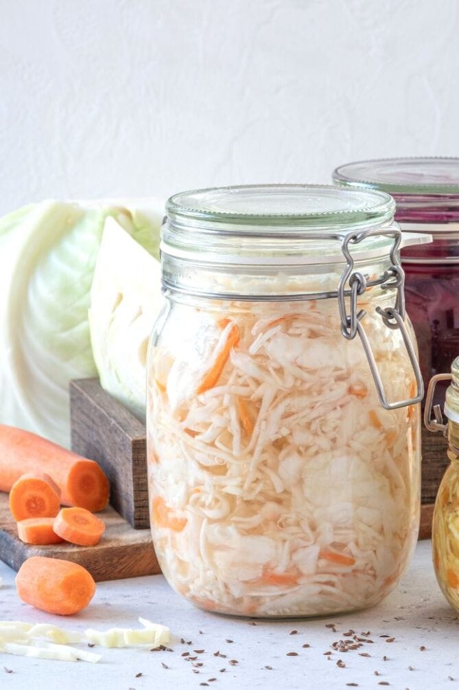 A jar of sauerkraut with carrots and cabbage on the background. | MakeSauerkraut.com