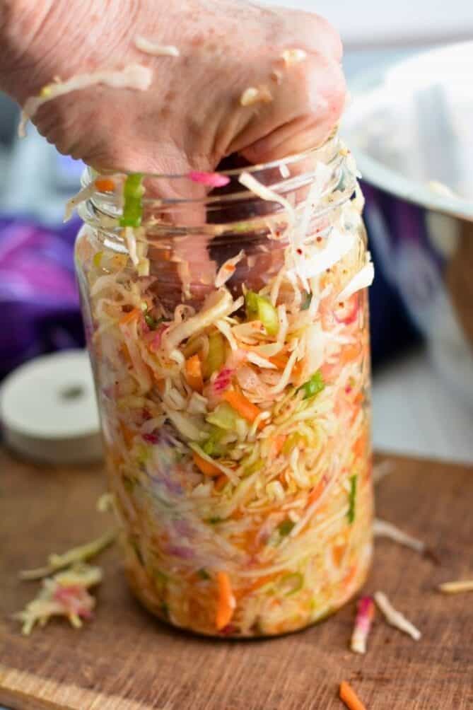 Woman packing a jar with sliced cabbage and grated carrot mixture for making sauerkraut. | MakeSauerkraut.com.